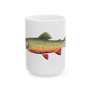 Könnte beinhalten: Weißer Keramikbecher mit einer detaillierten Illustration einer Bachforelle. Der Fisch hat einen gesprenkelten grün-gelben Körper, rote Flossen und eine schwarz-weiße Rückenflosse. Ein dekorativer Artikel für Angler.