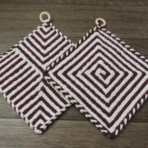 May include: Two white and burgundy striped pot holders with wooden rings. The pot holders have a square shape and a crocheted design.