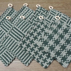 Peut inclure: Ensemble de huit maniques tissées vertes et blanches avec des anneaux en bois. Les maniques ont des motifs géométriques différents.