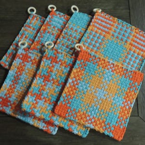 May include: Set of six woven pot holders in orange, blue and white with a chequered pattern. Each pot holder has a white ring attached to the top.