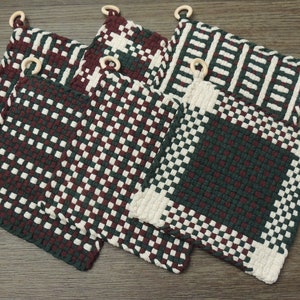 Peut inclure: Ensemble de dessous de plat carrés tissés, aux motifs et couleurs variés. Les dessous de plat présentent un mélange de teintes bordeaux, blanches et vertes, avec des anneaux en bois pour les suspendre. Le design tissé ajoute une touche texturée.