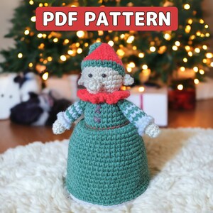 May include: Crochet pattern for a Christmas elf doll. The elf is wearing a green dress, a red hat, and a white and red striped scarf. The pattern is available as a PDF download.