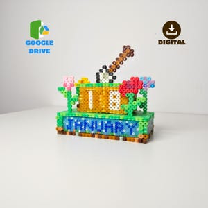 Puede incluir: Un calendario colorido y hecho a mano con pequeñas cuentas. El calendario muestra la fecha "18" y el mes "ENERO". También se incluyen flores decorativas y un elemento en forma de guitarra. Las palabras "GOOGLE DRIVE" y "DIGITAL" también son visibles.