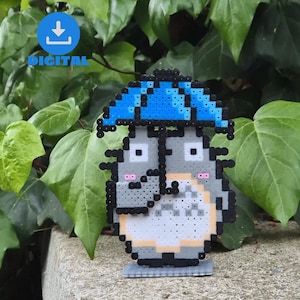 Könnte beinhalten: Eine graue und weiße Pixel-Art-Figur mit einem blauen Regenschirm. Die Figur hat große Augen und einen kleinen Mund. Die Figur steht auf einem grauen Sockel.