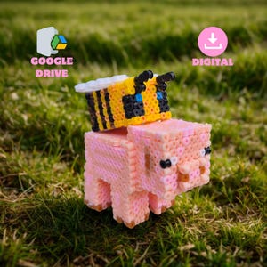 May include: A pixelated pink pig with a yellow and black bee on its back, made from small, colorful beads. The pig has small black eyes and a brown snout. The bee has black antennae and white wings. The background is green grass.