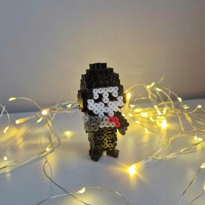 Könnte beinhalten: Eine dreidimensionale Pixel-Art-Figur aus schwarzen, weißen, grauen und roten Kunststoff-Bügelperlen. Die Figur hat einen schwarzen Kopf und Körper, ein weißes maskenartiges Gesicht sowie kleine rote und graue Akzente auf der Vorderseite.