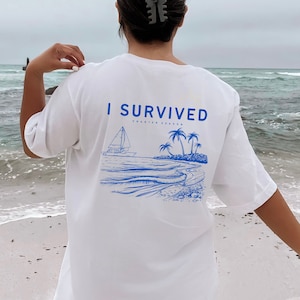 May include: White t-shirt with blue text that reads "I Survived Charter Season" and a blue illustration of a sailboat, palm trees, and waves.