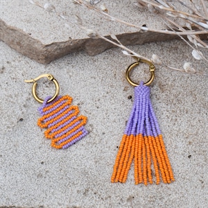 May include: A pair of beaded earrings with a purple and orange color scheme. One earring is a tassel style and the other is a geometric shape.