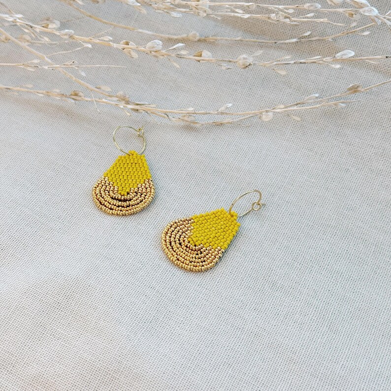 May include: A pair of gold hoop earrings with yellow and gold beaded teardrop dangles.