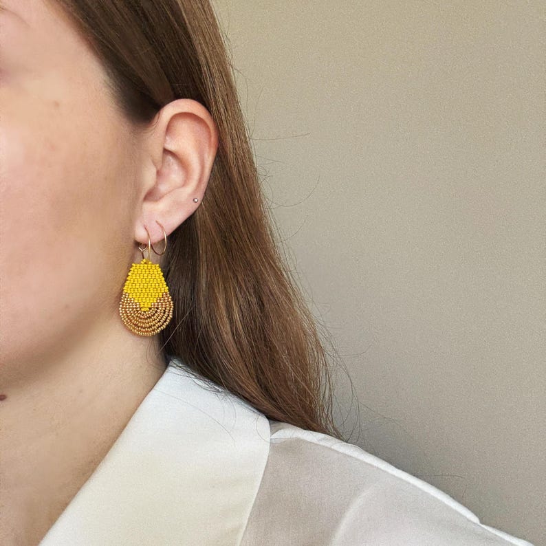 May include: A pair of yellow and brown teardrop-shaped beaded earrings. The earrings are made of small beads and have a gold-toned metal hook.