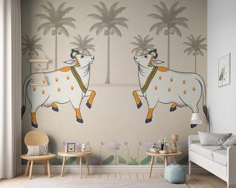 May include: A beige wall mural with two white cows with orange accents and brown palm trees. The mural is in a room with a white couch, two wooden chairs, and two wooden side tables.