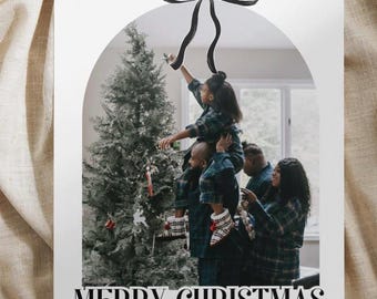 May include: A Christmas card with a photo of a family decorating a Christmas tree. The card has a black bow at the top and the text "Merry Christmas" and "Love, The Maucks".