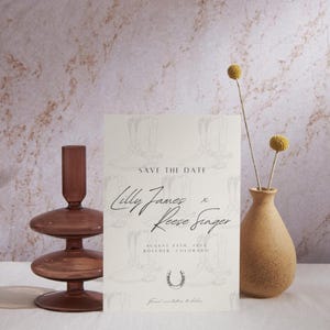 Peut inclure: Carte de sauvegarde de la date avec un fond blanc et un motif de bottes de cowboy. Le texte indique "Save the Date" "Lilly James" "Reese Singer" "August 24th, 2024" "Boulder, Colorado" et "Formal invitation to follow".