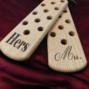 May include: Two wooden paddles with holes and leather straps. The top paddle is engraved with the word "Hers" and the bottom paddle is engraved with the word "Mrs."