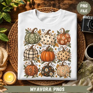 Peut inclure: Un t-shirt blanc avec une impression graphique de neuf citrouilles aux motifs et couleurs variés, incluant des carreaux, des pois, des cœurs et des motifs floraux, entourées de petites feuilles, d'étoiles et de cœurs disposés en grille.