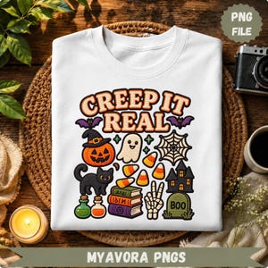Peut inclure: Un t-shirt blanc avec un motif coloré sur le thème d'Halloween portant l'inscription "CREEP IT REAL". Le design comprend une citrouille, un fantôme, un chat noir, des bonbons, une toile d'araignée, des livres, une main squelette et une tombe.