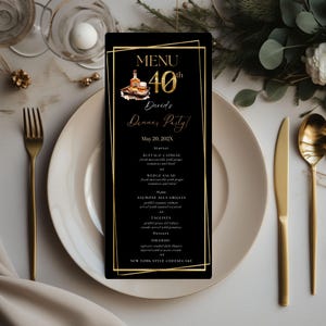 Op de afbeelding: Een zwart menukaart met gouden tekst en een gouden rand ligt op een wit bord. Het menu is voor een 40e verjaardagsdiner en bevat de menu-items. Een gouden vork, mes en lepel liggen op tafel.
