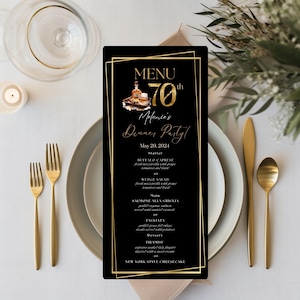 May include: A black menu card with gold text and a gold frame, set on a table with gold cutlery and white plates. The menu reads "MENU 70th Melanie's Dinner Party!" with a list of food items.