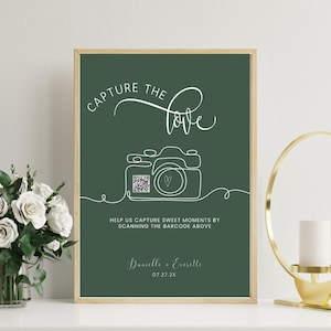 Könnte beinhalten: Gerahmter Druck mit dunkelgrünem Hintergrund und goldfarbenem Rand. Der weiße Text lautet "CAPTURE the love" über einer Strichzeichnung einer Kamera. Darunter steht der Text "HELP US CAPTURE SWEET MOMENTS BY SCANNING THE BARCODE ABOVE".