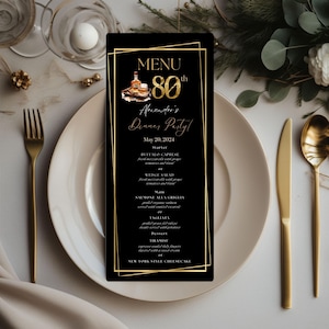 Könnte beinhalten: Eine schwarze Menükarte mit goldenen Akzenten für ein 80. Geburtstagsdinner. Die Speisekarte umfasst Vorspeisen, Hauptgerichte und Desserts. Die Karte liegt auf einem weißen Teller mit goldenem Besteck.