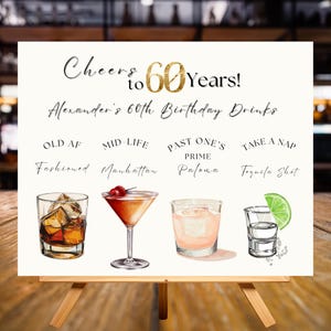 以下が含まれることがあります： 木製のイーゼルに立てられた白い看板。テキストは「Cheers to 60 Years!」と「Alexander's 60th Birthday Drinks」です。 「Old AF Fashioned」や「Tequila Shot」など、カクテルのイラストが描かれています。