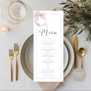 May include: A wedding menu with a watercolor illustration of a ring with a pink ribbon. The menu includes a starter, salad, main course, dessert, and a note that matching menus are available for purchase.