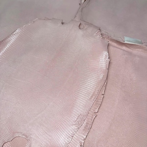 May include: Multiple pieces of pale pink leather with a distinct, fine-grained, reptilian-style embossed texture. The material is cut into irregular, organic shapes with visible edges and a consistent light pink colour throughout the surface.
