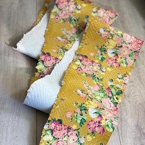 May include: Mustard yellow leather strips with a floral pattern of pink and white roses and green leaves. The underside of the leather is white. The leather has a snakeskin texture.