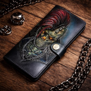 May include: Black leather wallet with a detailed embossed design of a creature with red hair and glowing orange eyes. The wallet has a snap closure and a decorative button. A metal chain and other accessories are in the background.