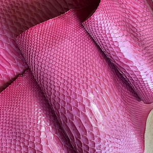 May include: A vibrant magenta snakeskin leather hide featuring a distinct, raised scale pattern across the entire surface. The material displays a glossy finish with deep, saturated pink tones and a flexible, organic texture throughout the piece.