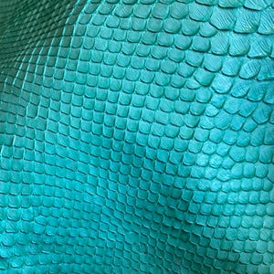 May include: A textured material featuring a repeating pattern of small, overlapping scales in a vibrant teal color. The surface displays a consistent, organic grid-like structure with subtle variations in light and shadow across the folds.