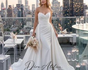 Vestido de novia de satén estilo sirena, con escote corazón, hombros descubiertos y cola desmontable.