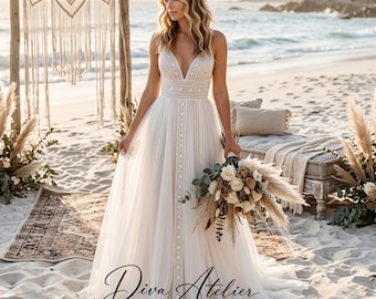 May include: A floor-length white wedding dress with a deep V-neckline, spaghetti straps, and intricate geometric lace detailing along the bodice and center skirt. The dress features a flowing tulle skirt and is held with a bouquet of dried flowers.
