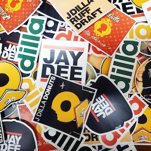 May include: A collection of colourful stickers featuring the names "Jay Dee" and "J Dilla" with various designs, including a doughnut, a plane, and a record.