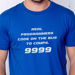 Op de afbeelding: Koningsblauw T-shirt met witte tekst: "REAL PROGRAMMERS CODE ON THE BUS TO COMPS. 9999". Het shirt met korte mouwen is gemaakt van zacht materiaal. De tekst staat in het midden op de voorkant.