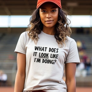 May include: A white t-shirt with black text that reads "What does it look like I'm doing?"