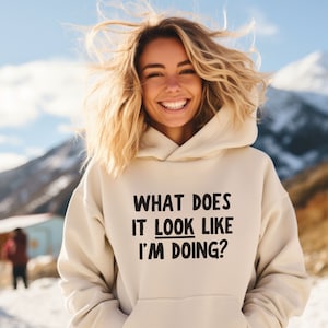 May include: A cream-coloured hoodie with black text that reads "What does it look like I'm doing?"