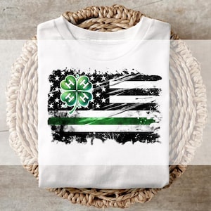 May include: White t-shirt with a distressed American flag design. The design includes a green shamrock with four green "H" letters, a green stripe, and black and white stars and stripes, suitable for St. Patrick's Day.
