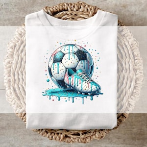 May include: White t-shirt with a colourful illustration of a football and a football boot. The football is black, white, and blue, and the boot is white and blue with a drippy design. The design includes sprinkles and drips.