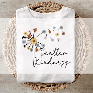 May include: White t-shirt featuring a dandelion graphic and the text "Scatter Kindness". The dandelion is made up of small flowers in shades of yellow, orange, brown, blue, and white.