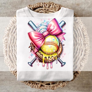Könnte beinhalten: Ein weißes T-Shirt mit einem Grafikdesign aus einer rosa Schleife, einem Softball und zwei Baseballschlägern. Der Softball ist gelb mit weißen Nähten und tropft mit rosa und weißem Zuckerguss. Die Schläger sind hinter dem Softball und der Schleife gekreuzt.
