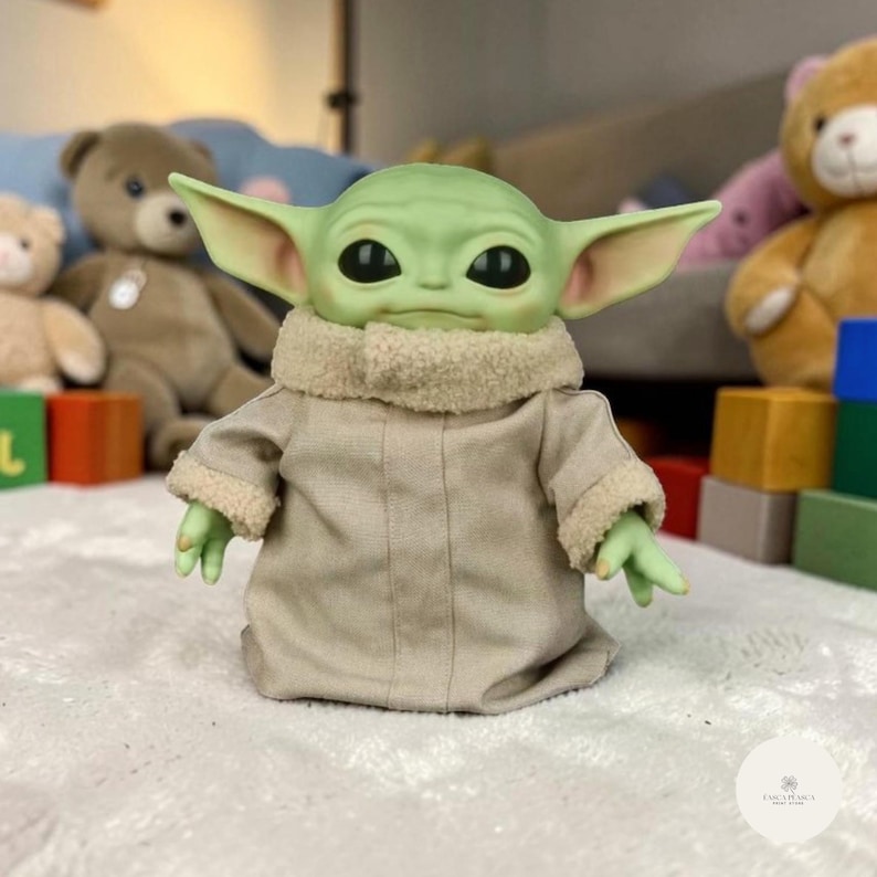 Puede incluir: Mu&ntilde;eco de piel verde con orejas grandes, ojos negros y una t&uacute;nica color beige. El mu&ntilde;eco tiene un cuello color beige y peque&ntilde;as manos verdes. El mu&ntilde;eco es un personaje de una popular franquicia de ciencia ficci&oacute;n. Es un objeto de colecci&oacute;n.