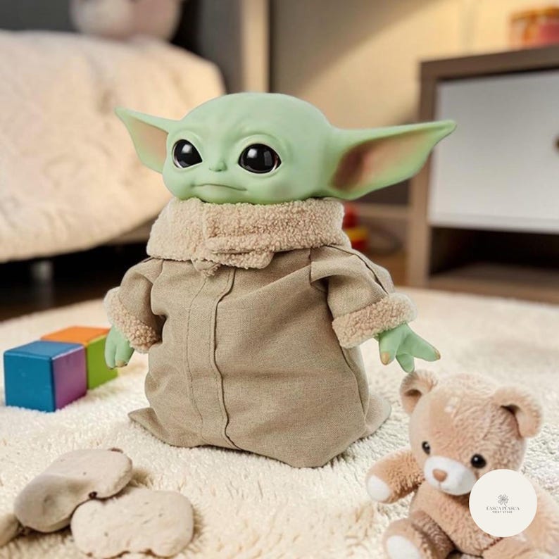 Puede incluir: Mu&ntilde;eco de piel verde con grandes ojos negros y orejas puntiagudas, que lleva un abrigo color canela con cuello y pu&ntilde;os afelpados. El mu&ntilde;eco es un personaje de una popular serie de ciencia ficci&oacute;n. Est&aacute; sentado en una alfombra blanca con un osito de peluche y bloques de colores.