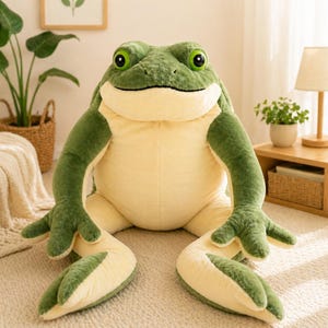 Puede incluir: Un peluche grande de rana con un exterior texturizado de color verde oscuro en la espalda y las extremidades, contrastado por una barriga y parte inferior de color crema suave. La rana tiene ojos redondos de color verde brillante.