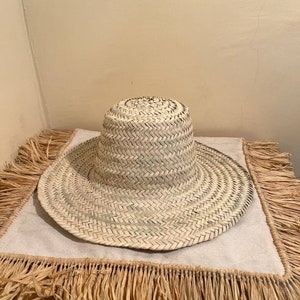 May include: A wide-brimmed straw hat with a woven design. The hat is light brown and has a slightly rounded crown.