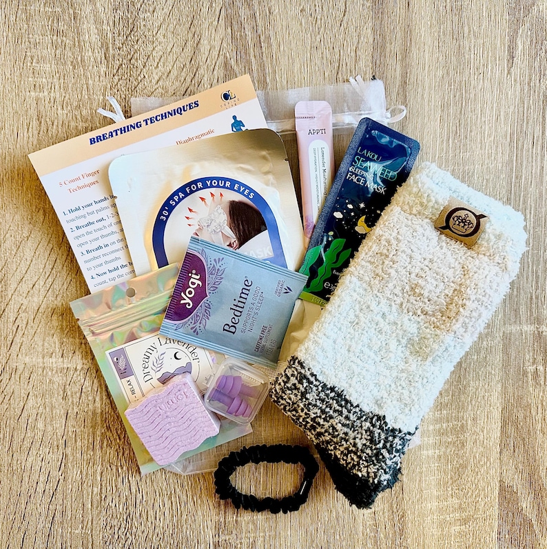 May include: A selection of relaxation items, including a face mask, eye mask, tea, fluffy socks, and a hair tie. The image also shows a small bag of lavender-scented items, a nail separator, and a leaflet on breathing techniques.