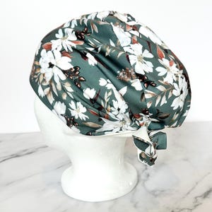May include: A green scrub hat with a white floral pattern. The hat is tied at the back with a bow.