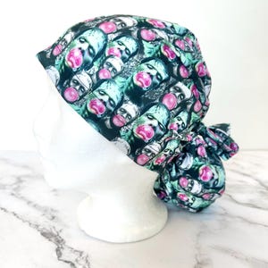 May include: A scrub cap featuring a repeating pattern of green-toned zombie faces, each blowing a bright pink bubble with bubblegum. The fabric head covering has a gathered back section with ties, displaying a consistent graphic print throughout.