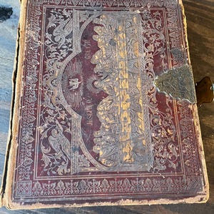 May include: A vintage, leather-bound book with a gold-embossed design depicting the Last Supper. The book has a decorative metal clasp and is in a worn condition.