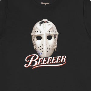 Op de afbeelding: Zwart t-shirt met een wit hockey goalie masker en het Philadelphia Flyers logo. Onder het masker staat het woord "Beeeeer" in een scriptlettertype met een rode onderstreping. Het shirt is gemaakt van een zacht materiaal.